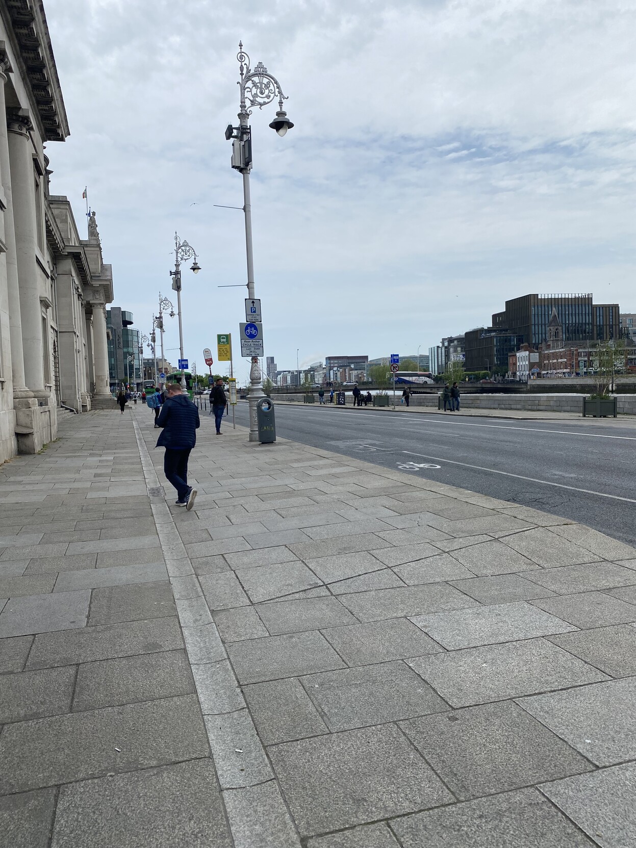 Footpath scene at Custom House Quay. Empty roadway and buildings at far side of river in the background 