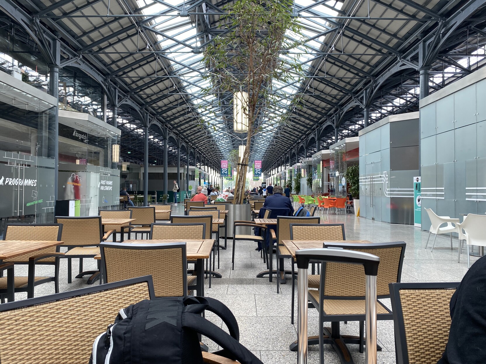 Interior mall of CHQ. Dining tables and chairs, and mall roof of metal and glass in view