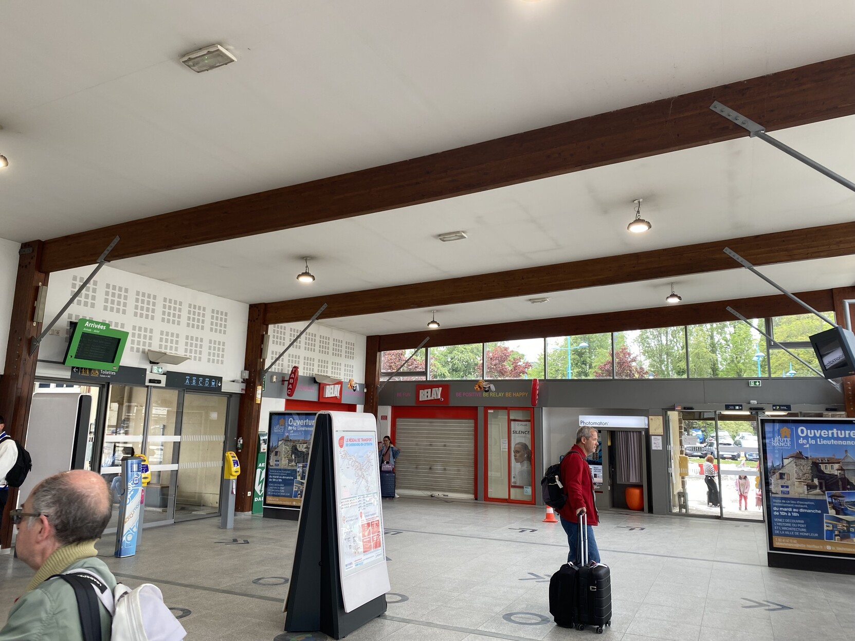 Entrance to train station in Cherbourg. Closed retail in corner. Passenger with suitcase in the foreground