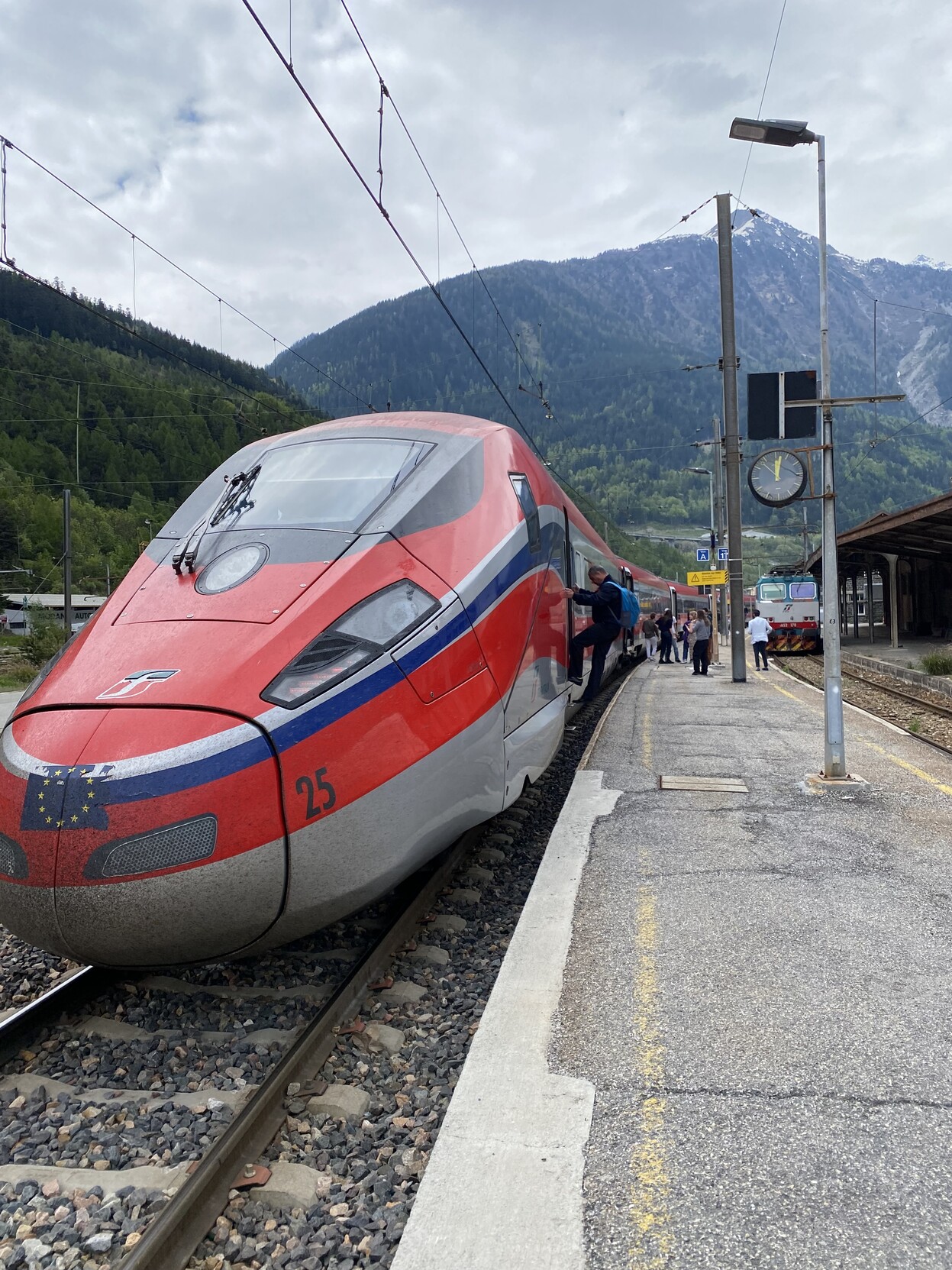 Red Frecciarossa high speed train at platform in Modane. Views from the front with snow tipped mountain in the background.