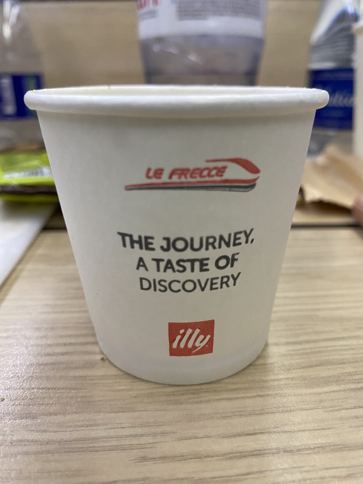 White single use paper espresso cup with Le Frecce and Illy branding, and the message: The journey, a taste of discovery.