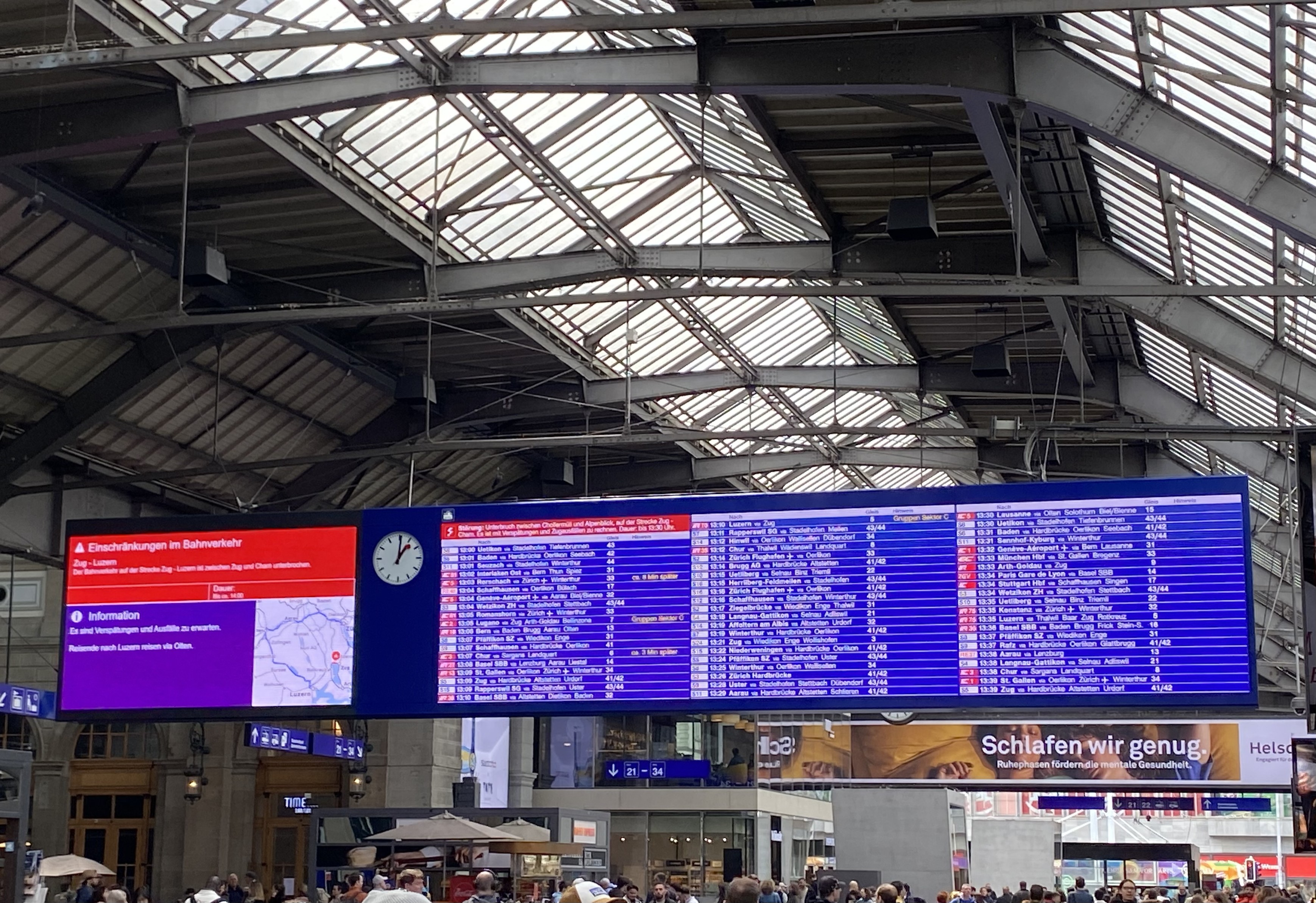 Departure board at Zürich HB three columns of departures are displayed in white text on a blue background. To their left an analogue clock and to its left an information column in red and blue displaying details of a disruption near Luzern.