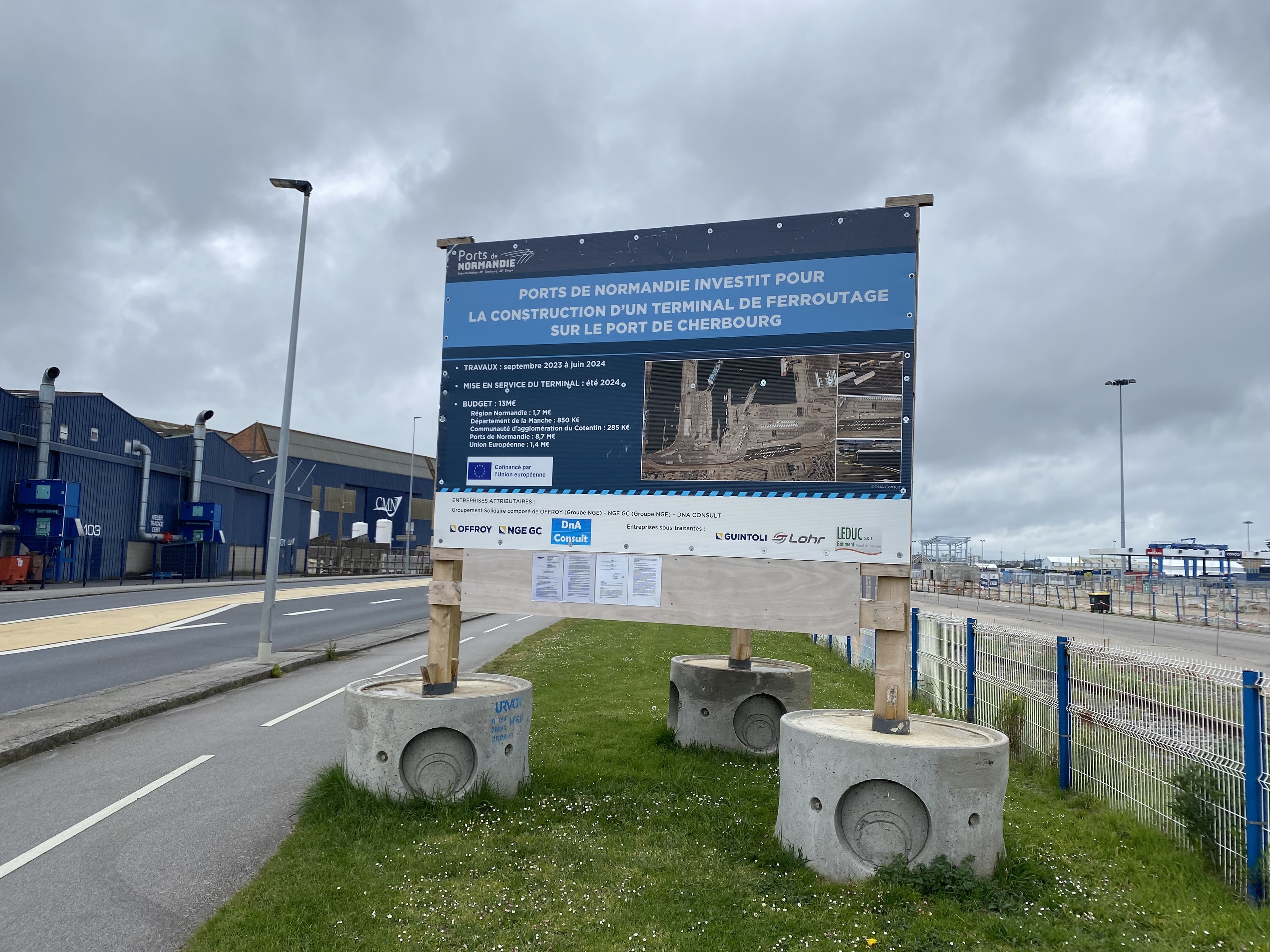 A large sign mostly in blue with white lettering. The primary information reads in French : “PORTS DE NORMANDIE INVESTIT POUR LA CONSTRUCTION D