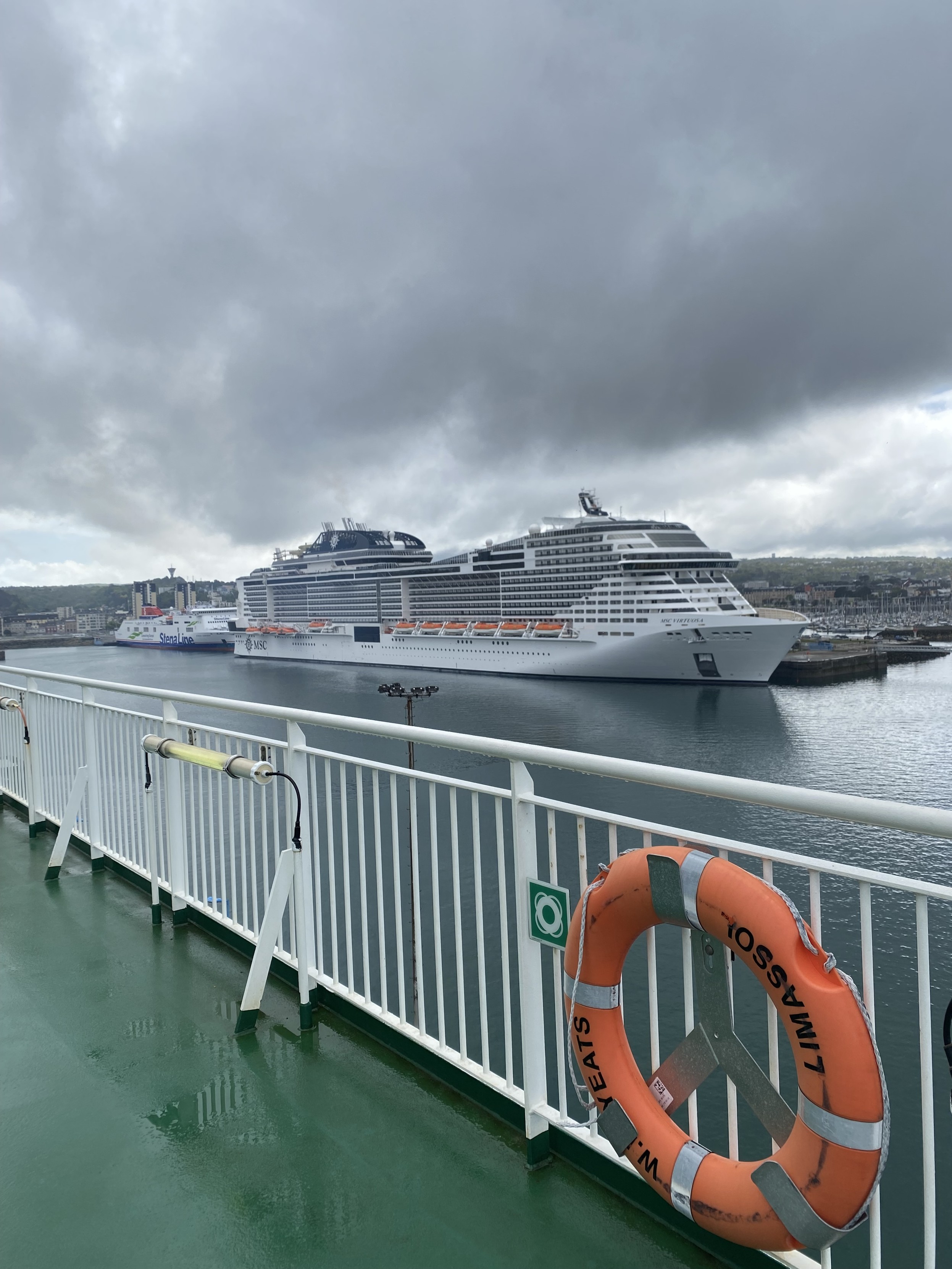 A view from the green floored deck of the Irish Ferries WB Yeats at berth in Cherbourg. A huge cruise ship and a small Stena car ferry  can be seen at another berth. The sky is cloudy and grey.