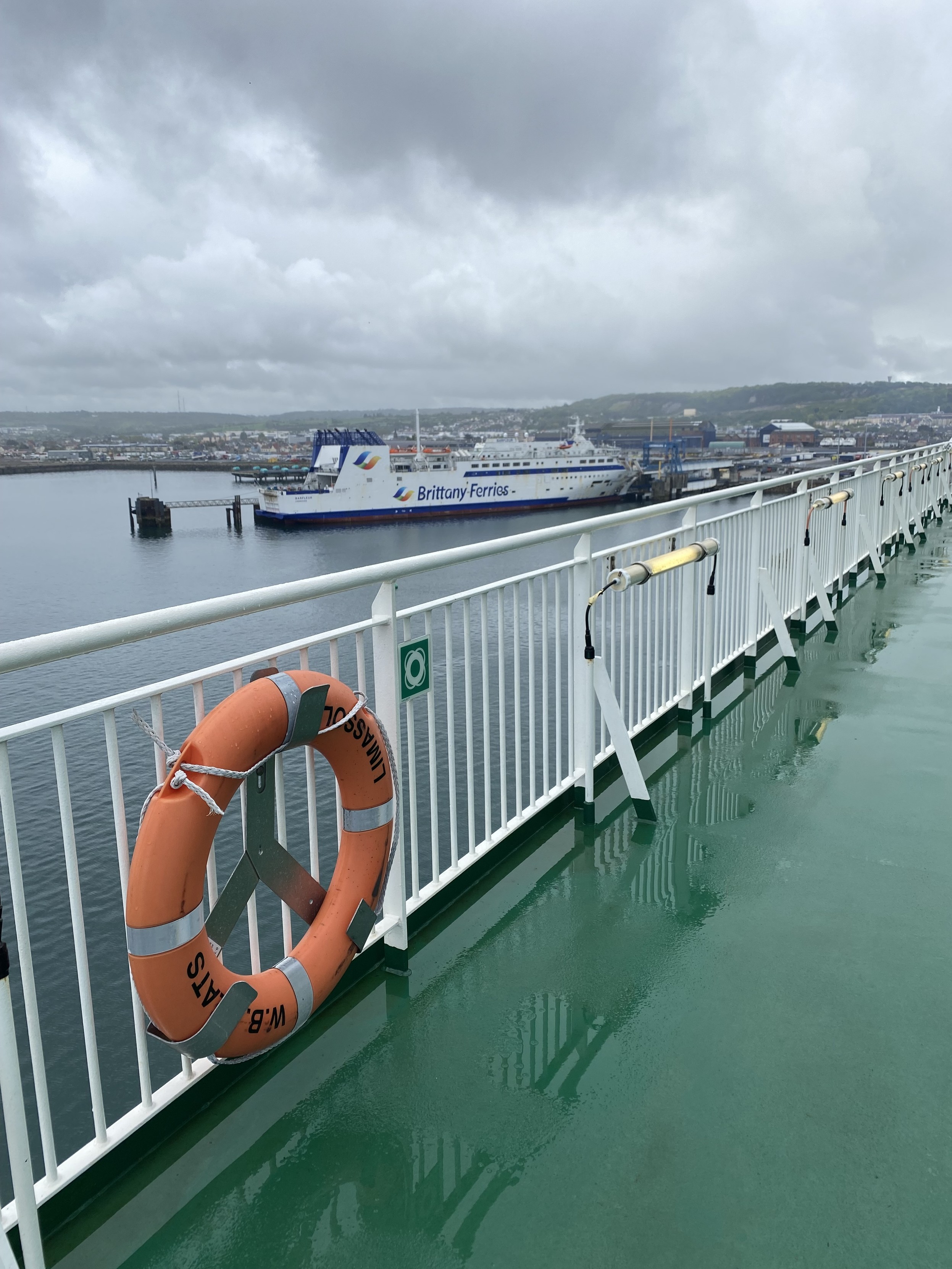 A view from the green floored deck of the Irish Ferries WB Yeats.  A Brittany Ferries car ferry can be seen at another berth. The sky is cloudy and grey.